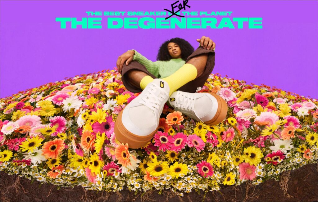 A woman is sitting in a field of flowers with a pair of sneakers.